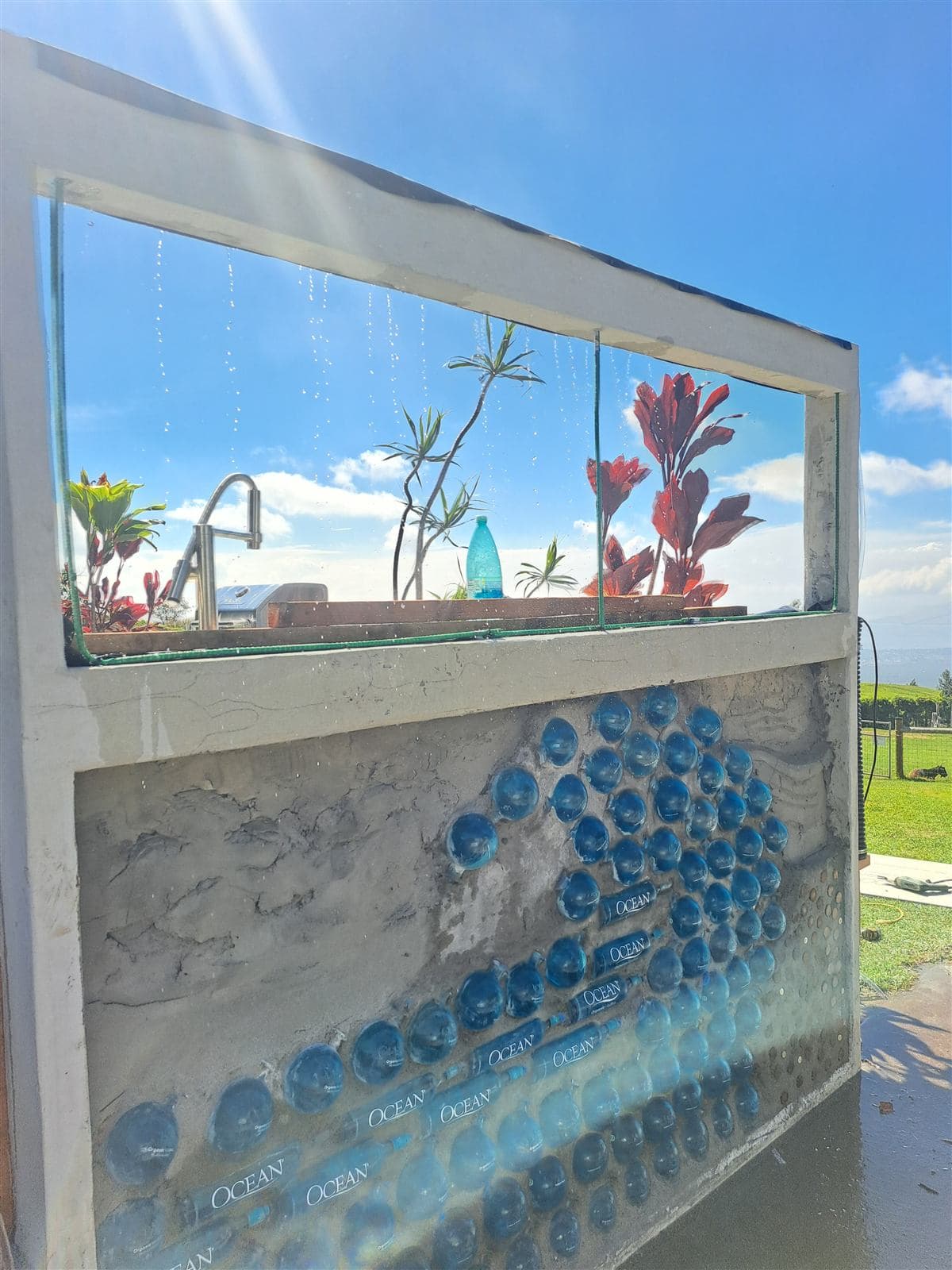 Outdoor bar wall with blue glass bottles set into the concrete below a glass window