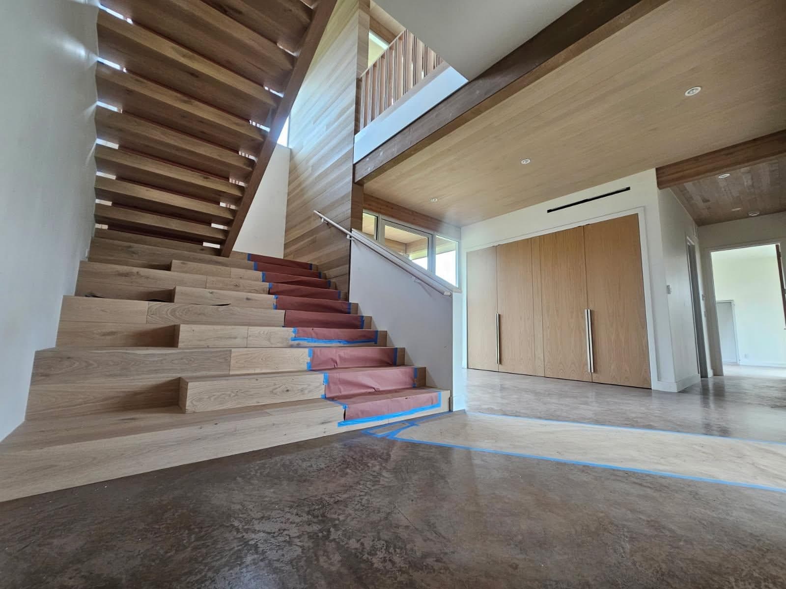 White oak staircase with open treads and wood-paneled wall, protective paper still on the steps